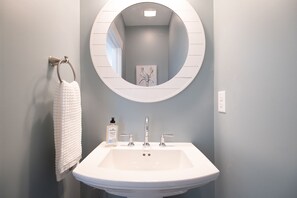Une salle de bain avec un lavabo blanc, un miroir rond et un porte-serviettes.