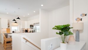 A modern kitchen with white cabinetry, a central island, pendant lighting, and a potted plant on the counter.