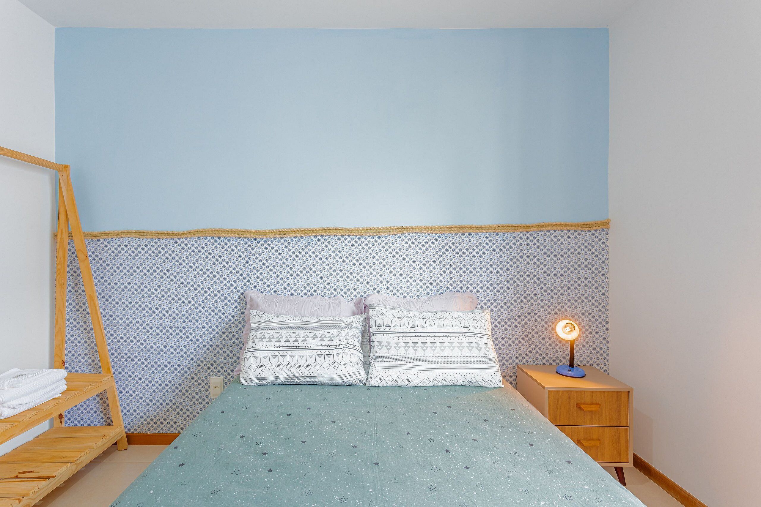 Un dormitorio con una litera, dos almohadas, una mesita de noche con lámpara y papel tapiz estampado.