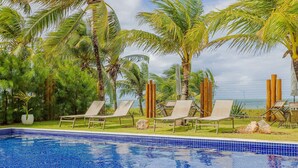 A swimming pool with lounge chairs and palm trees. - IT57 Apto Pé na Areia - Praia da Espera (Camaçari)