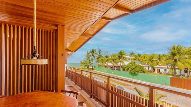 A wooden balcony with a view of palm trees and a road. - IT57 Apto Pé na Areia - Praia da Espera (Camaçari)