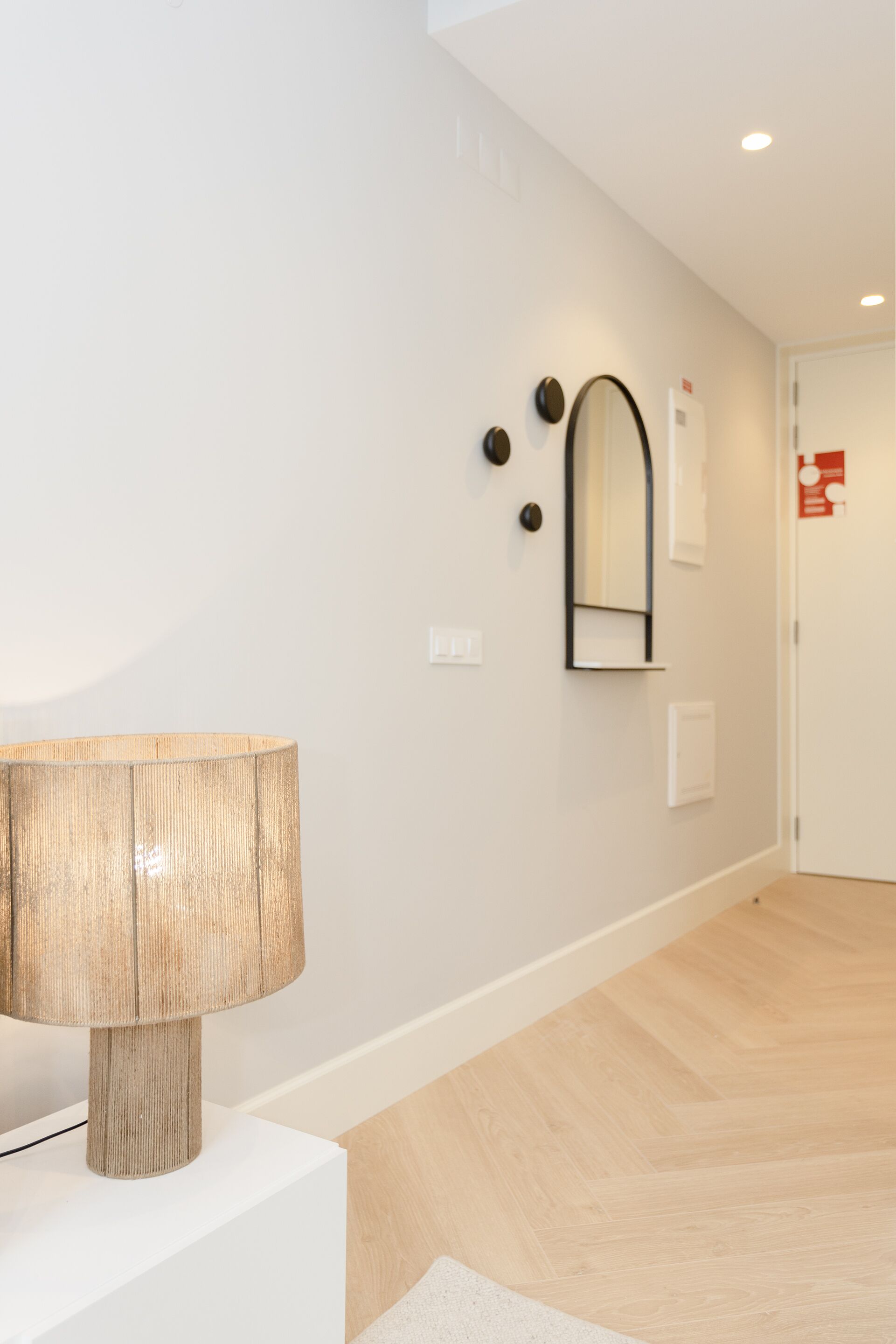 Ein modernes Interieur mit einer Lampe auf einem weißen Sockel, einem Spiegel an der Wand und einem Holzboden.