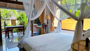 Ein Zimmer mit einem Bett, einem Tisch, Stühlen, einem Ventilator und Blick auf Grünfläche.