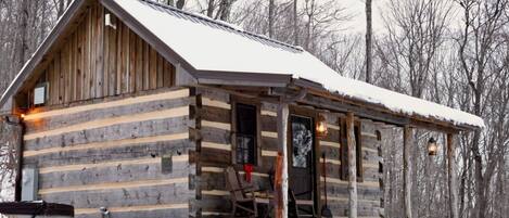 Une cabane en rondins avec une véranda, une porte et une fenêtre.