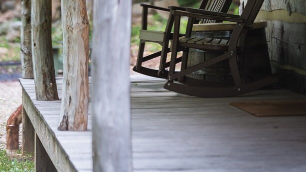 A rustic wooden porch with a rocking chair, lanterns, and a view of a forest.