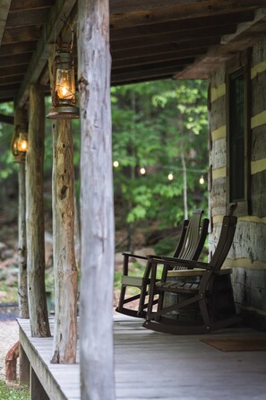 A rustic wooden porch with a rocking chair, lanterns, and a view of a forest. - Log Cabin w HotTub near Seneca Rocks & Spruce Knob (Riverton)