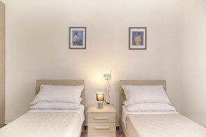 A double room with two beds, a bedside table with a lamp, and two framed pictures on the wall.