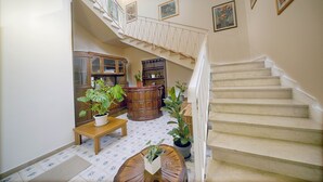 Un vestíbulo amplio con una imponente escalera, un mostrador de recepción de madera y diversas plantas en macetas.