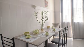Un comedor con una mesa dispuesta para cuatro, sillas, un florero con plantas y una ventana con cortinas.