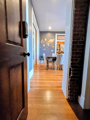 Un couloir au plancher de bois menant à une salle à manger équipée d’une table et de chaises.
