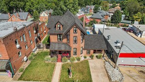 A two-story brick house with a front porch, a small front yard, and a red garage. - Studio + 3rd Floor Access (Washington)