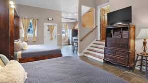 A bedroom with two beds, a TV, a dresser, and a staircase leading to another room. - Studio + 3rd Floor Access (Washington)