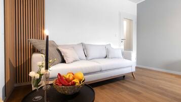 A modern living room with a white sofa, a round black coffee table, a wicker fruit basket, and a tall candle.