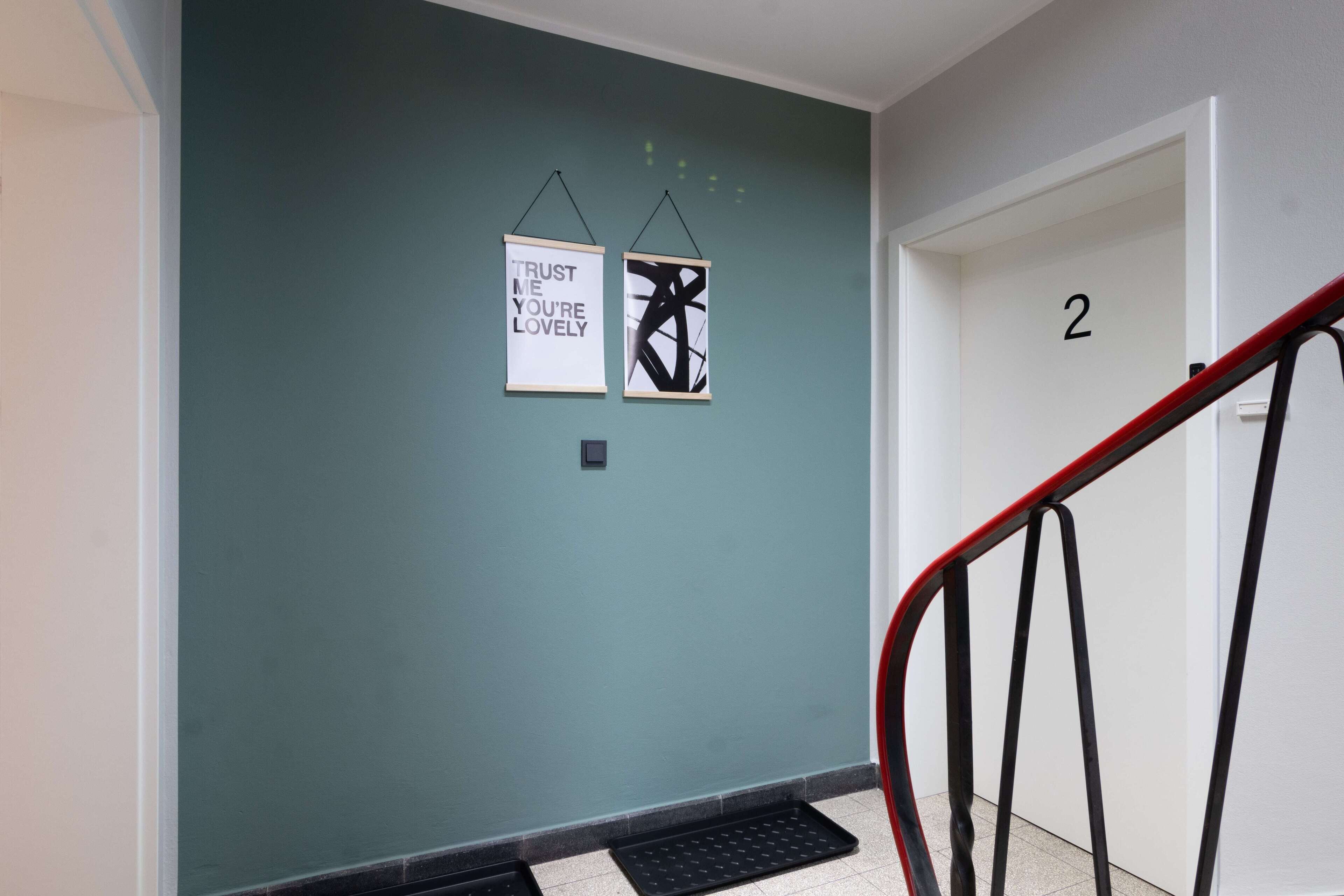 A hallway with teal walls, two framed motivational posters, a black metal handrail, and a door labeled with the number 2.