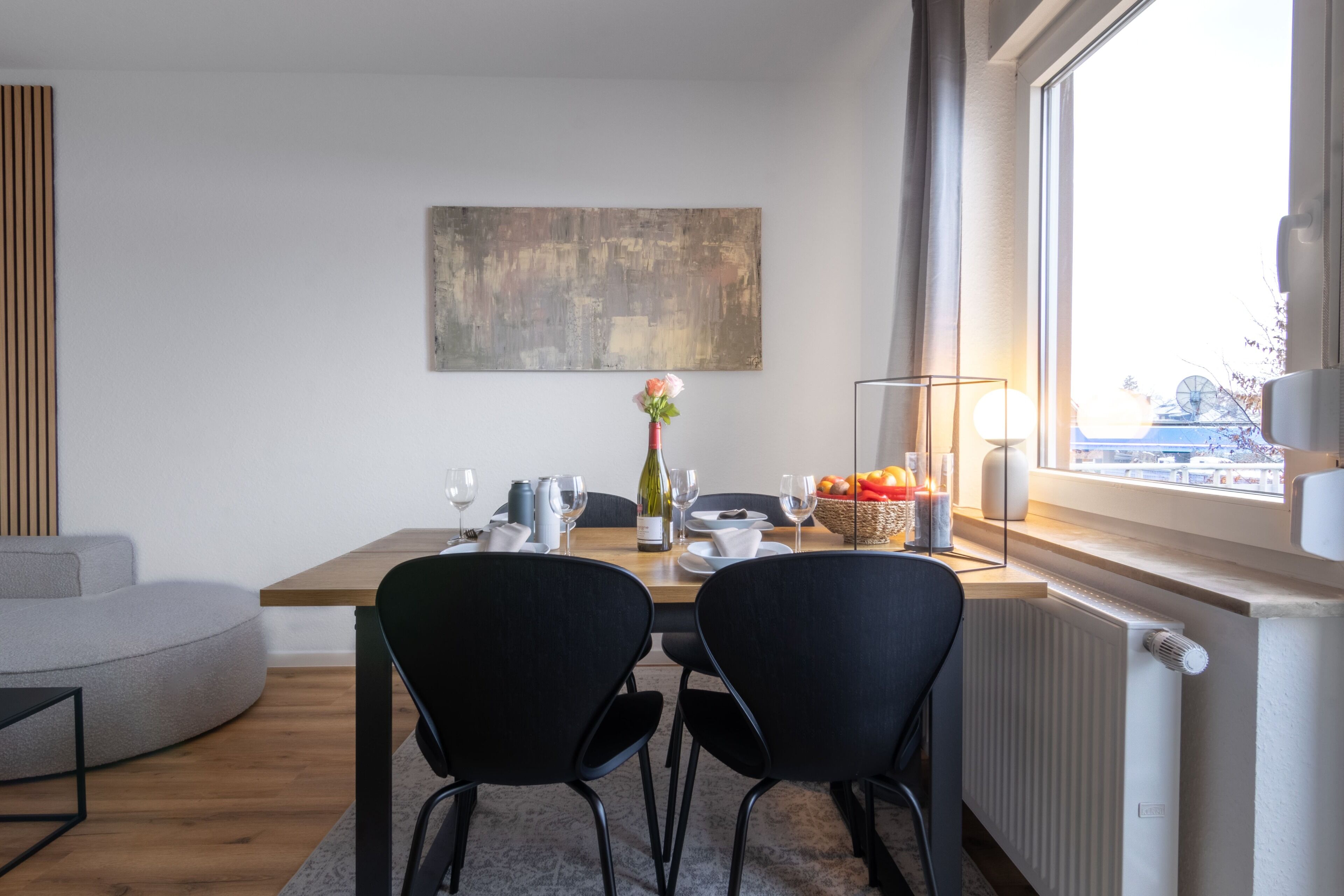 A modern dining area with a wooden table, black chairs, and a vase with flowers.