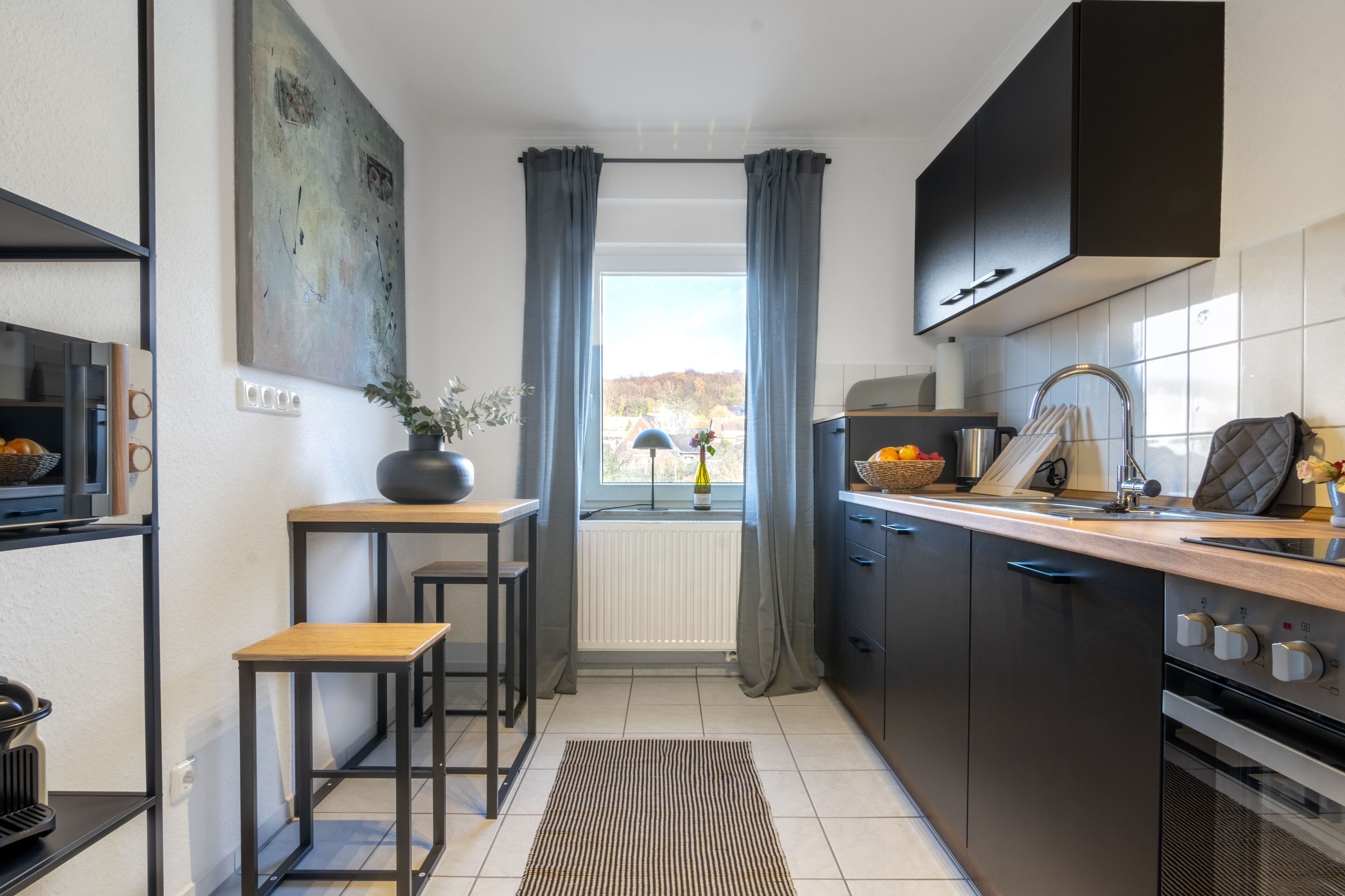 Una cocina moderna con gabinetes negros, horno empotrado y una ventana con cortinas.
