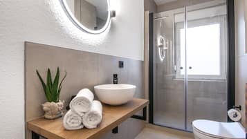 A modern bathroom with a wooden vanity, a large mirror, a white sink, and a glass shower enclosure.