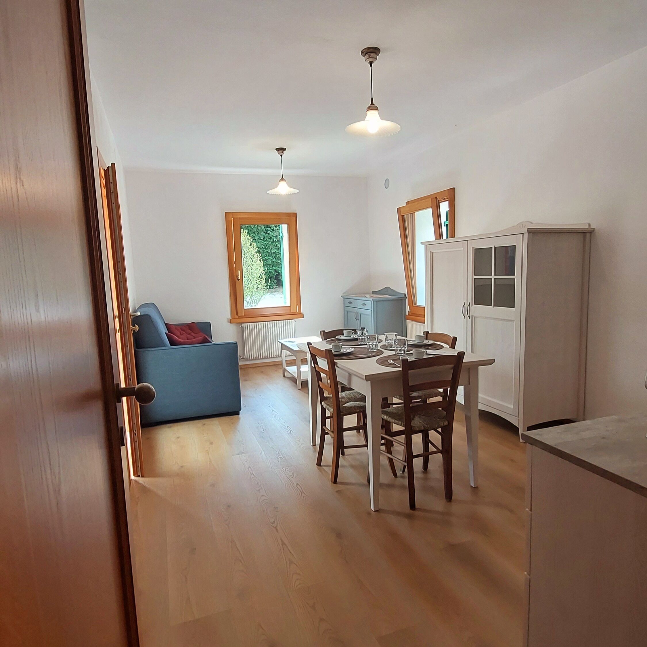 A compact kitchen with a dining area, a blue sofa, and a window with a view of greenery.