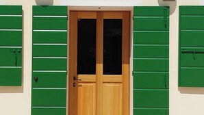Una puerta de madera con contraventanas verdes, dos luces fijadas a la pared y un buzón con el número 28.