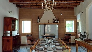 Un comedor con una larga mesa de madera dispuesta para una comida, una araña y una cocina al fondo.