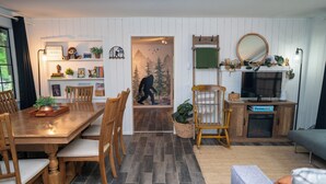 A cozy living room with a wooden dining table, chairs, a sofa, and a fireplace. - Bigfoot Bungalow — Creekside Paradise (Hoodsport)