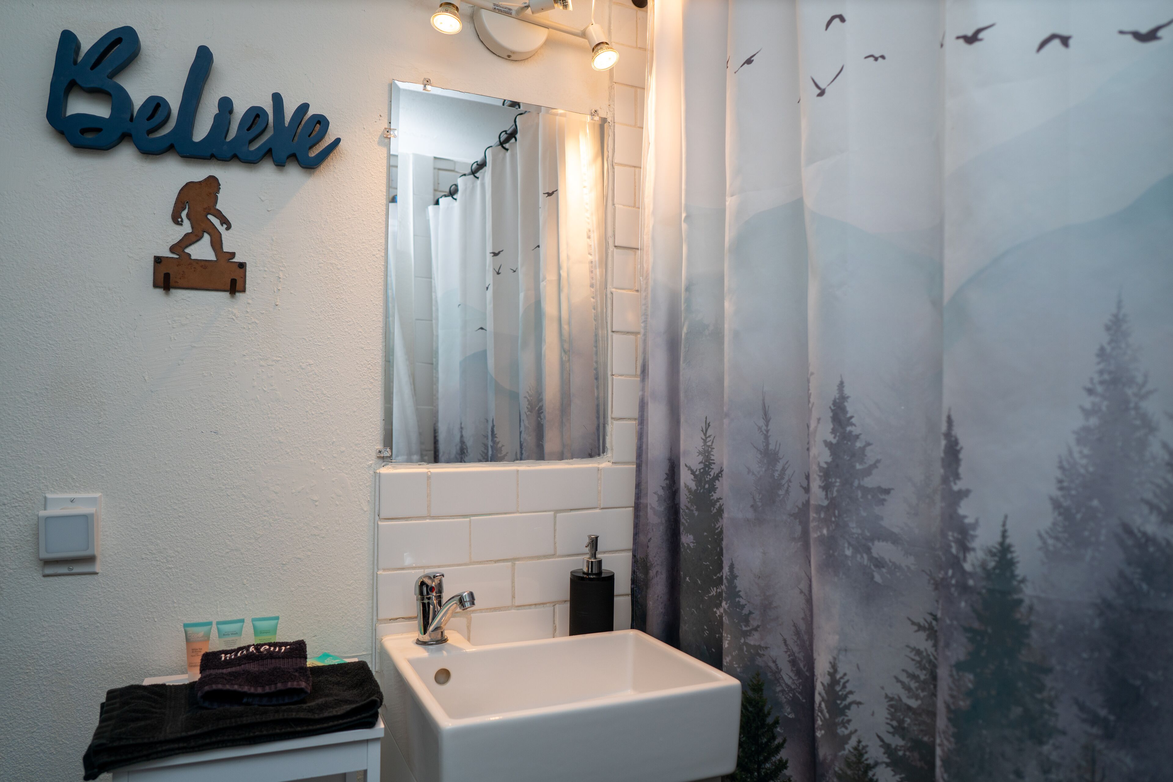 A bathroom with a white sink, a mirror, and a 'Believe' sign.
