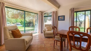 Habitació àmplia amb una finestra gran, un sofà, una taula de menjador amb caires i una cadira amb coixí.
