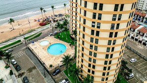 A high-rise hotel with a pool, beach view, and parking area. - Beira Mar Caragua (Caraguatatuba)