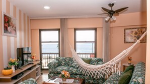 A living room with a sofa, a coffee table, a TV, and a hammock. There are windows with a view of the sea. - Beira Mar Caragua (Caraguatatuba)