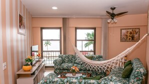 A room with a hammock, a sofa, a coffee table, and a view of palm trees. - Beira Mar Caragua (Caraguatatuba)