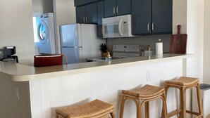 Eine moderne Küche mit dunkelblauen Schränken, einer weißen Kücheninsel mit Barhocker, einer Mikrowelle und einem Einbauofen.