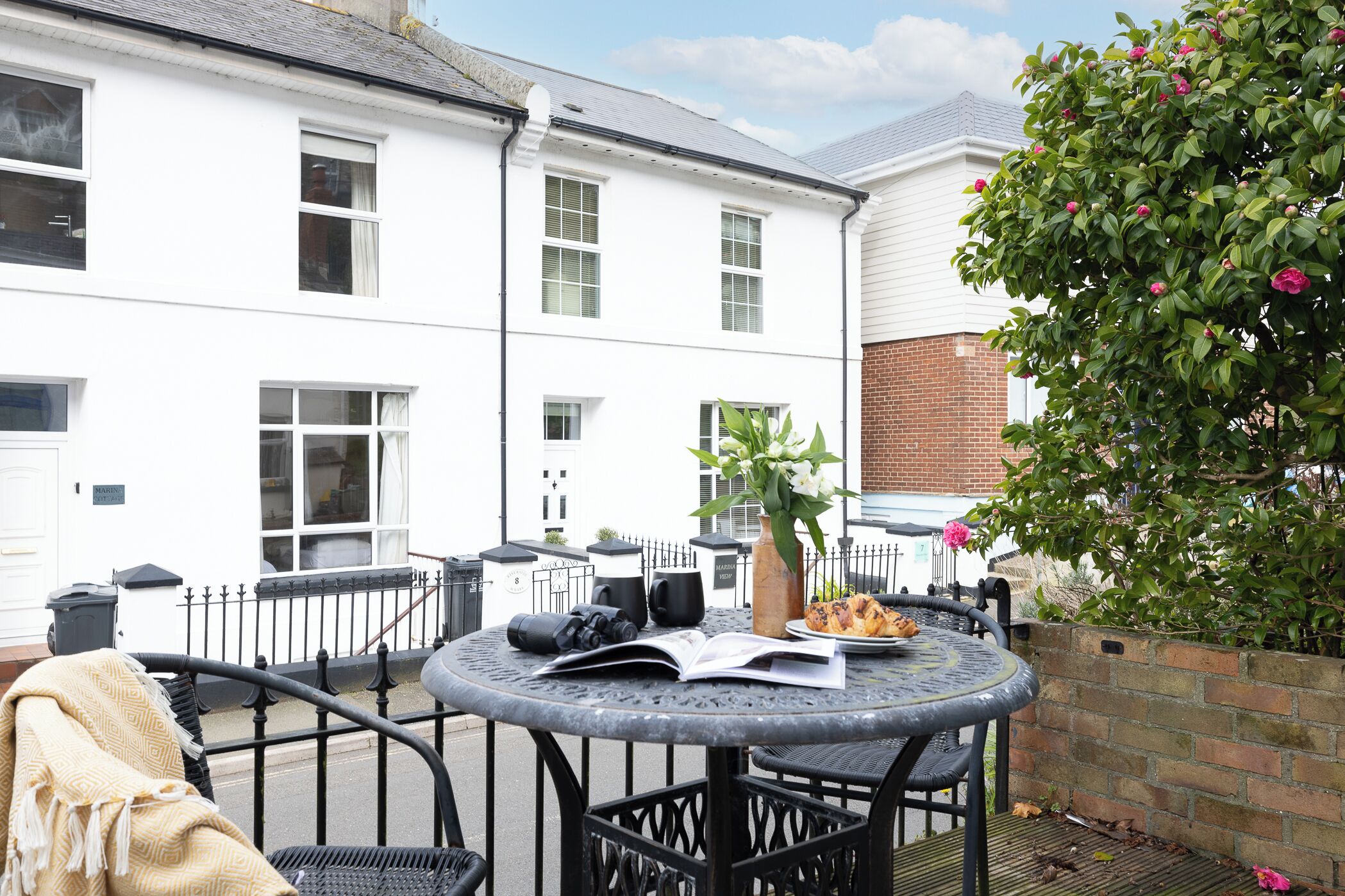 A patio with a round table, chairs, a book, binoculars, and a flower vase.