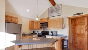 A kitchen with wooden cabinets, a stainless steel refrigerator, a microwave, and a large island with stools. - CDA River Condo: Fishing, Sleding, Floating, Skiing (Kingston)