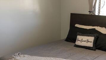 A neatly made bed with a grey blanket, a pillow with "Home Sweet Home" text, and two framed pictures on the wall.