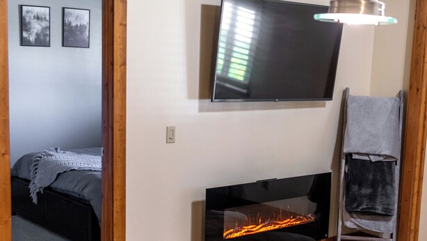 A kitchen with a wooden cabinet, a countertop, a hanging light fixture, a fireplace, and a television mounted on the wall. - CDA River Condo: Fishing, Sleding, Floating, Skiing (Kingston)