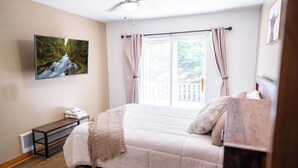 A bedroom with a bed, a TV mounted on the wall, a window with curtains, and a view of greenery outside. - CDA River Condo: Fishing, Sleding, Floating, Skiing (Kingston)