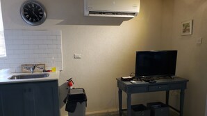 A compact kitchen with a sink, a clock, an air conditioner, a television, and a trash bin. - Almond Tree Studio - Modern A/C Apartment w/2 Queen beds in St. James (holetown)