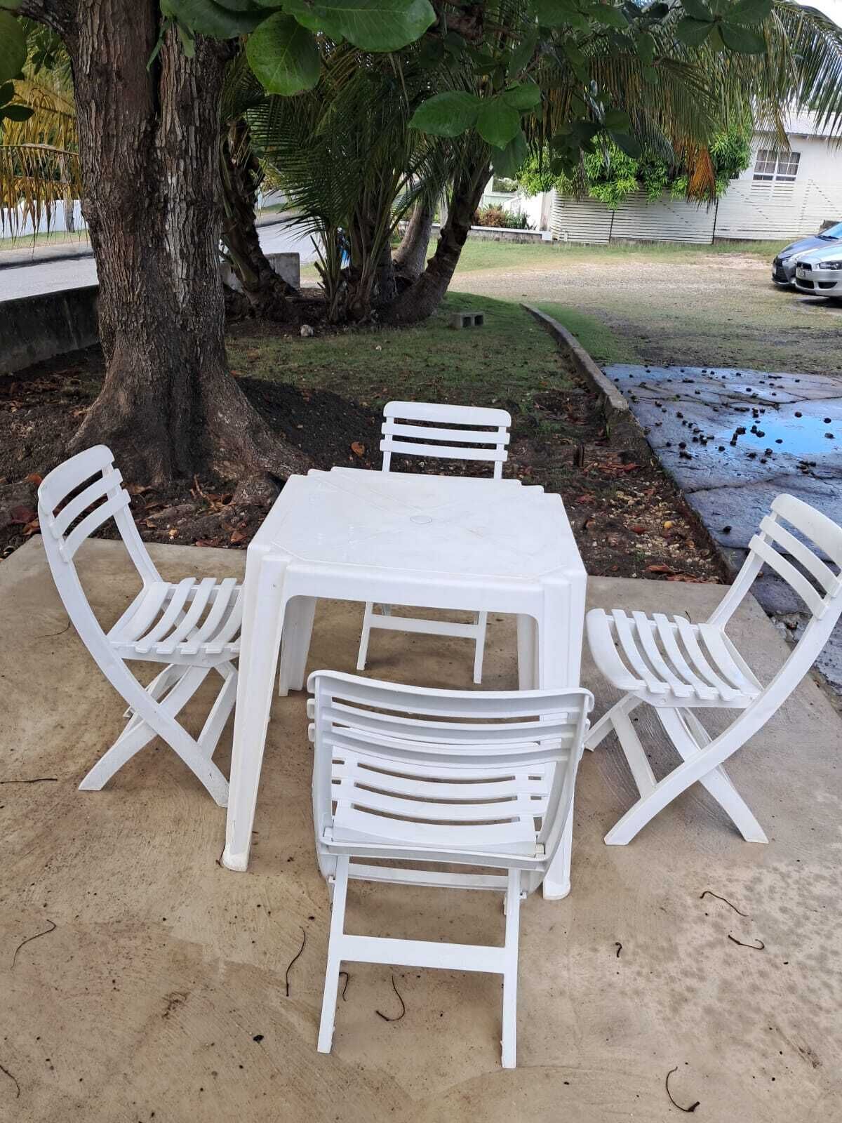 Een witte plastic tafel met vier bijpassende stoelen, buiten geplaatst onder een boom.