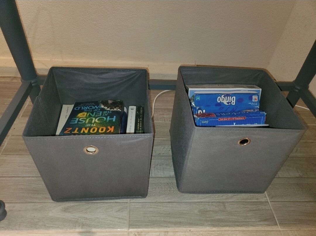 Two gray storage bins with books inside, placed on a wooden floor.
