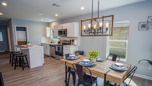 A modern kitchen with white cabinets, a central island, and a dining area with a wooden table and black chairs. - Charming 3br/1ba Close to Vibrant Downtown (San Antonio)