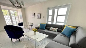 A modern living room with a grey sofa, a blue armchair, and a white coffee table. There are two framed pictures on the wall and a window with blinds. - Vistamar 5-bedroom Villa with pool (Carolina)