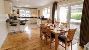 A modern kitchen with a dining area, wooden flooring, and large windows. - Gunn's Cottage (Enniskillen)