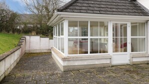A conservatory with a tiled roof and white walls, surrounded by a stone wall and a gravel path. - Gunn's Cottage (Enniskillen)