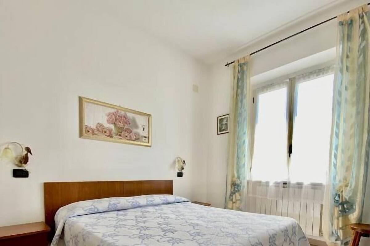 A bedroom with a bed, a wooden headboard, a framed picture on the wall, and a window with curtains.