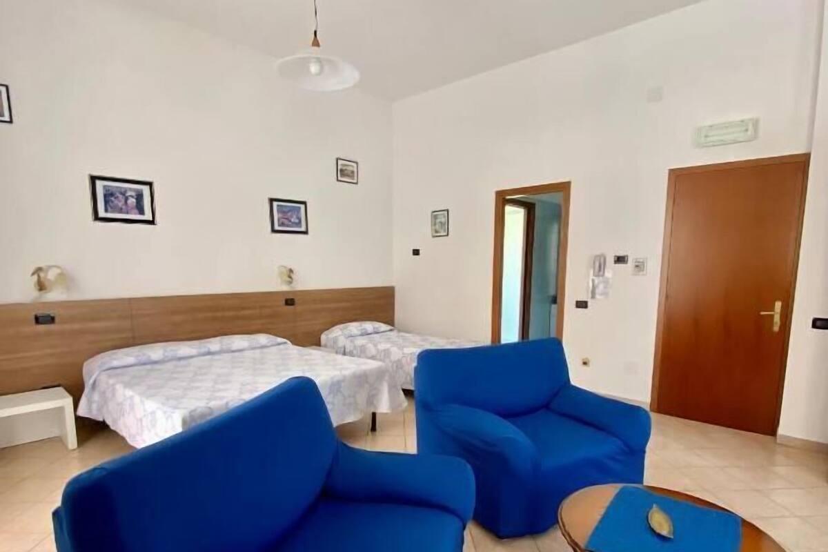 A hotel room with two single beds, a blue sofa, a small table, and a wooden door.