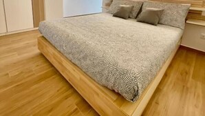 Une chambre moderne avec un cadre de lit en bois, une tête de lit à lattes et une fenêtre avec des rideaux.
