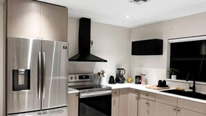 A modern kitchen with stainless steel appliances, a black range hood, and light wood cabinets. - Super Stylish 4BR Retreat in the Heart of Las Olas (Fort Lauderdale)