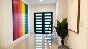 A hallway with a colorful abstract painting, a bench, a potted plant, and a door with a black frame. - Super Stylish 4BR Retreat in the Heart of Las Olas (Fort Lauderdale)