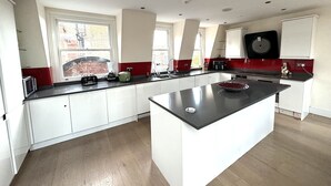 Una cocina moderna con armarios blancos, encimera negra y una isla grande. Hay ventanas que ofrecen luz natural y vistas al exterior.