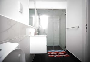 A modern bathroom with a white vanity, a glass shower enclosure, and a striped rug. - Ebs legend white limited (Accra)